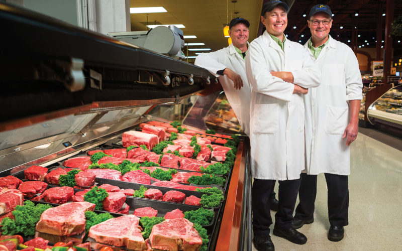 three meat butchers in front of meat case