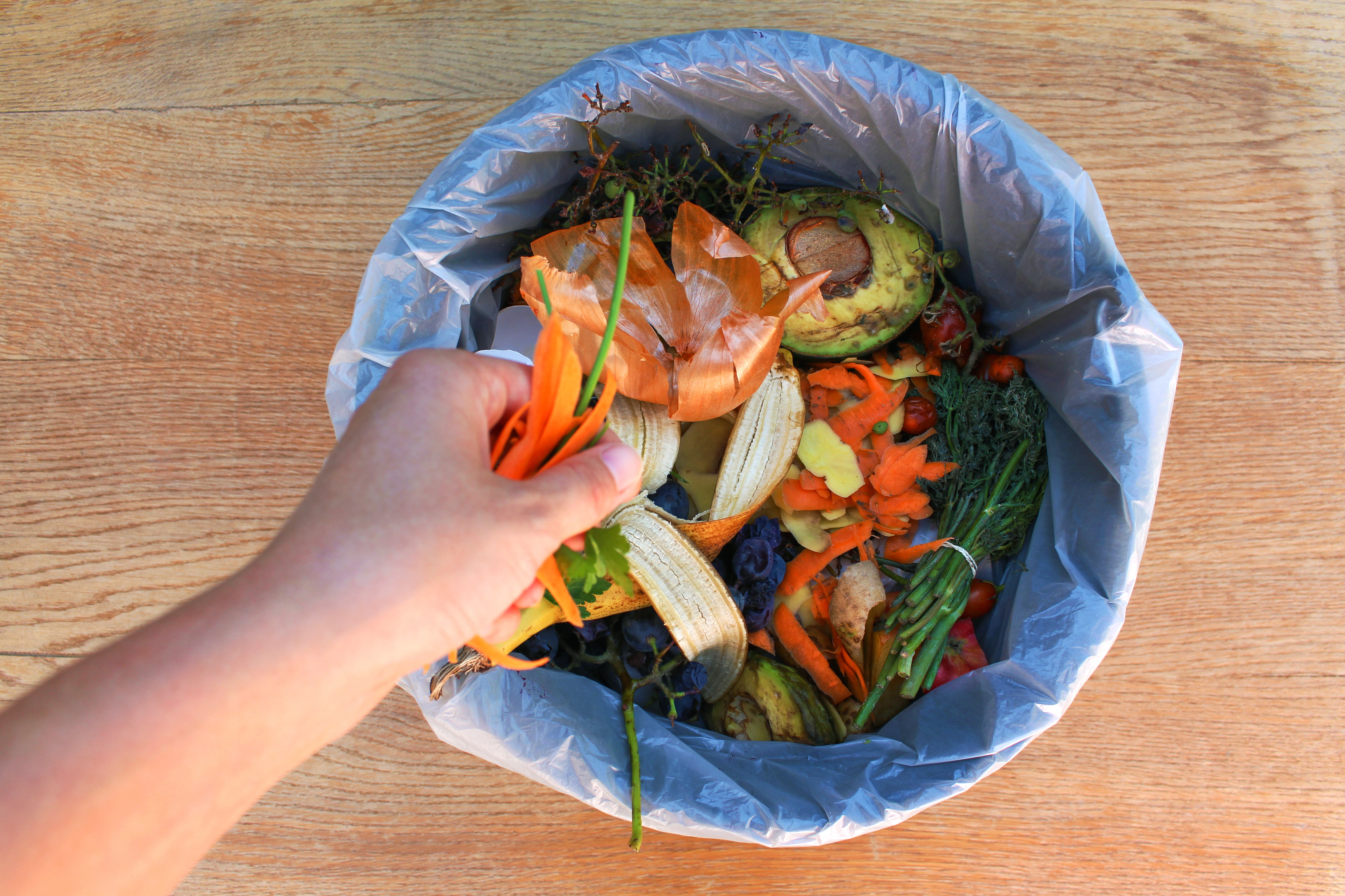 hand tossing fruit and vegetable food scraps into compost bin