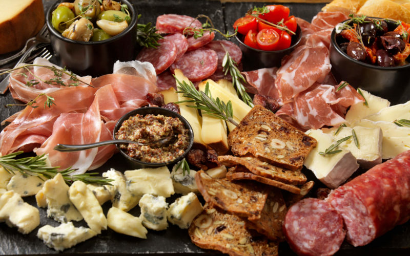 A cheese board complete with cheese, meat, bread, vegetables, and dips.