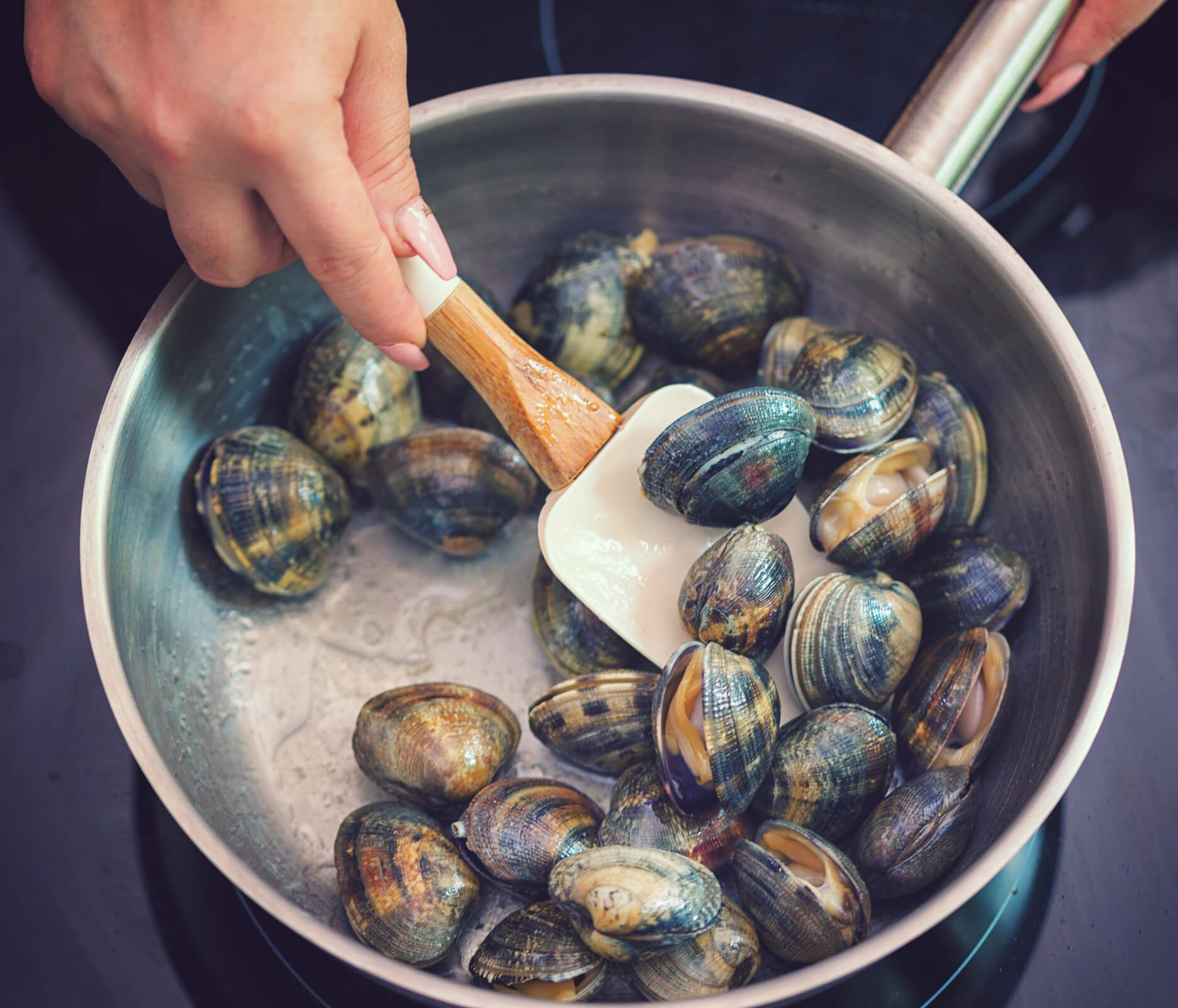 A woman cooks clams in a pot on the stove.