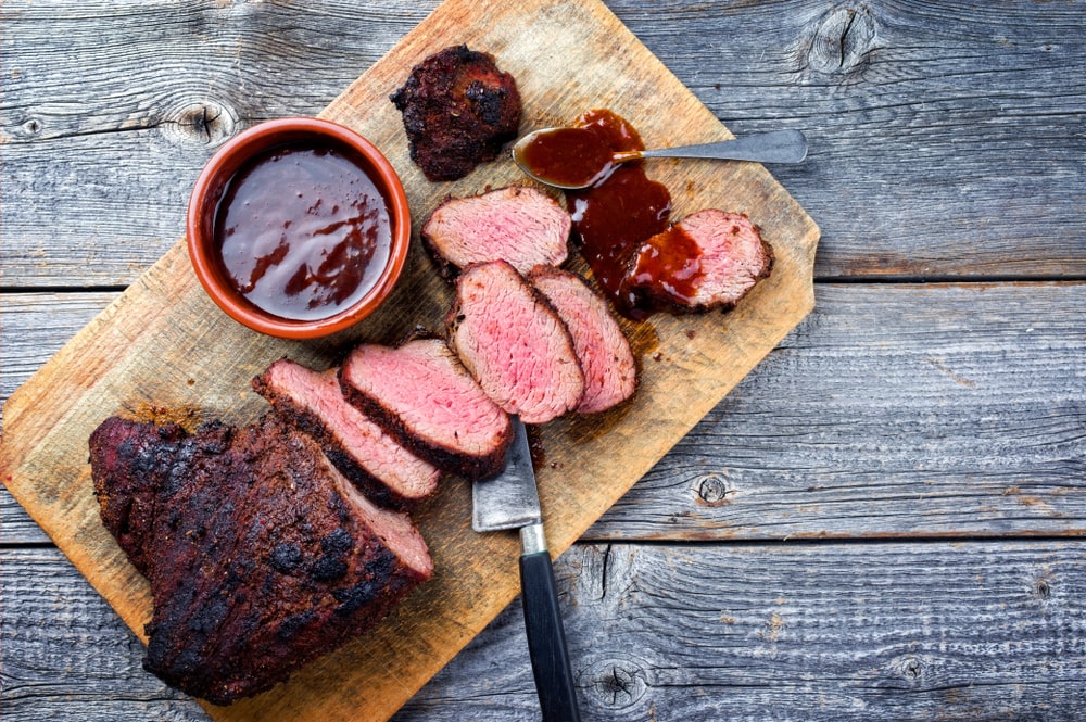 A bbq'd piece of meat on a cutting board with some bbq sauce adorning it. An example of dry rubbing and wet rubbing. 