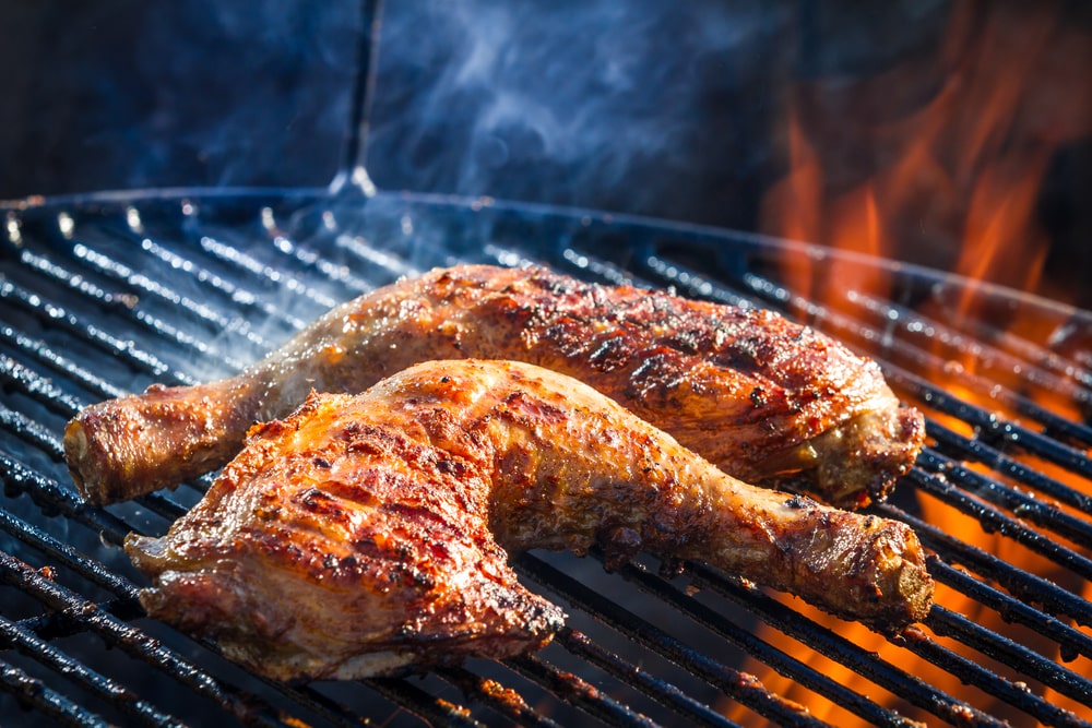 Chicken thighs cooking on a grill grate over a flame.