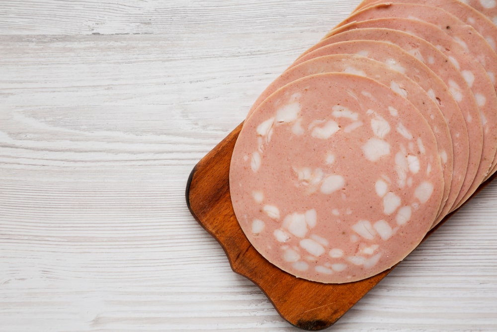 Multiple slices of bologna sliced up on a wooden charcuterie board