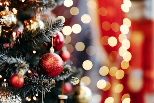 A close-up shot of a Christmas tree decorated with ornaments with blurred Christmas lights in the background.