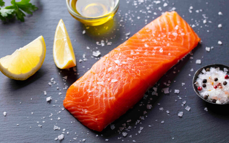 A Scottish salmon fillet sits on a black counter next to a few lemon slices