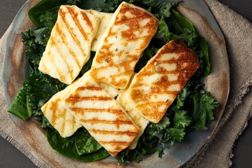 grilled halloumi cheese lays over a bed a greens