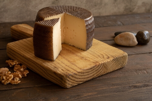 a wheel of manchego cheese sits on a cutting board