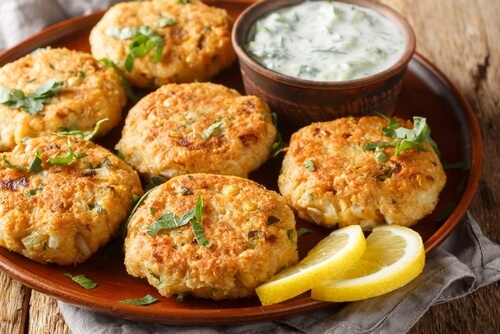 six crispy crab cakes sit on a red plate with dipping sauce